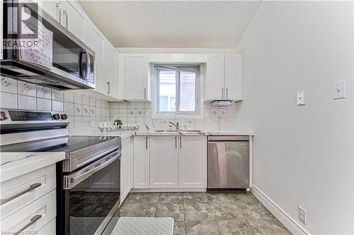 White cabinetry with modern hardware, stainless steel appliances, patterned backsplash, light-toned countertops, and tiled flooring - 168 Copper Leaf Street, Kitchener, ON 