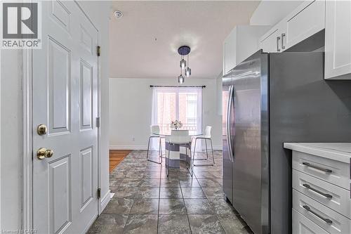 Tile flooring, white cabinetry, stainless steel refrigerator, white countertops, and modern pendant lighting - 168 Copper Leaf Street, Kitchener, ON 