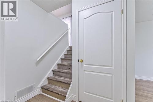 Wood-finish flooring, white panel door with brass hardware, and a staircase featuring a white handrail - 168 Copper Leaf Street, Kitchener, ON 