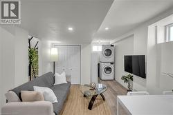 Living area with light wood-finish flooring, recessed lighting, and a stacked washer and dryer unit - 