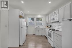 Bright kitchen featuring white cabinetry, subway tile backsplash, light-toned countertops, and wood-finish flooring - 