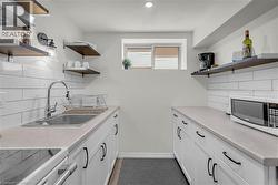 Lower Level Kitchen featuring white shaker-style cabinetry, a stainless steel sink with a high-arc faucet, and light-toned countertops - 