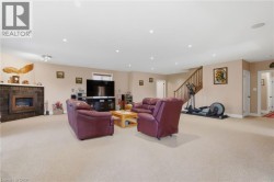 Spacious room featuring carpeting, recessed lighting, a built-in fireplace with a stone-finish surround, and a wood staircase - 
