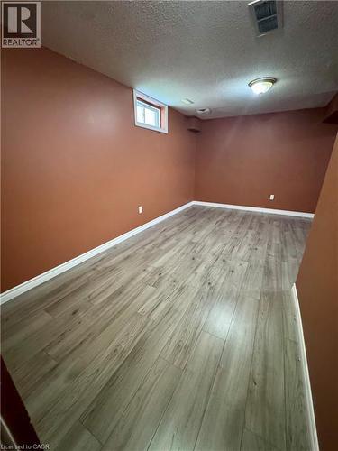 Spacious room featuring wood-finish flooring, warm-toned walls, a single window, and a flush-mount ceiling light fixture - 452 Beaumont Crescent, Kitchener, ON 