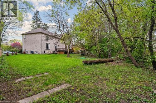 Spacious backyard featuring a sloped, grassy lawn, mature deciduous trees, and concrete stepping stones - 1541 Garnet Avenue, Mississauga, ON 