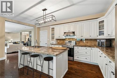 Gourmet kitchen featuring a central island with a sink, white cabinetry with dark hardware, stainless steel appliances, a tiled backsplash, and wood-finish flooring - 1541 Garnet Avenue, Mississauga, ON 