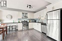 White cabinetry, stainless steel appliances, wood-finish flooring, black countertops, and a subway tile backsplash - 