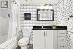White subway tile walls, wood-finish flooring, white vanity with black countertop, integrated sink, and bronze light fixture - 