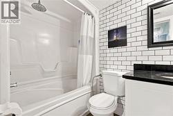 Subway tile accent wall, dark countertop vanity with integrated sink, white plumbing fixtures, and a shower/tub combination with a rain showerhead - 