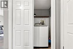 Compact laundry area featuring white subway tile, a wood-finish floating shelf, and a built-in top-load washing machine - 