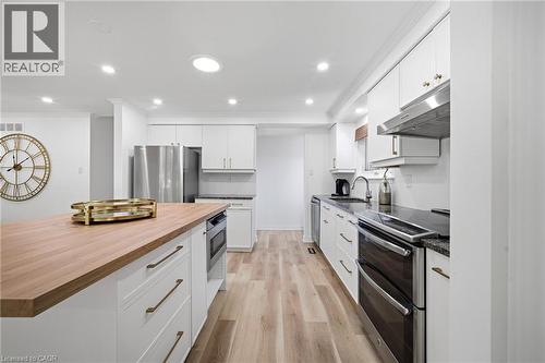 Modern kitchen featuring a wood-finish island countertop, white cabinetry with brushed gold hardware, and stainless steel appliances - 2306 Devon Road, Oakville, ON 