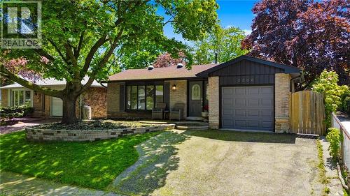Exterior featuring stone and vertical siding accents, a prominent front picture window, a single-car garage, and a mature front yard tree with a stone-bordered garden bed - 2306 Devon Road, Oakville, ON 