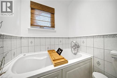 Corner bathtub with chrome fixtures, surrounded by white tiled walls with decorative accents - 2306 Devon Road, Oakville, ON 