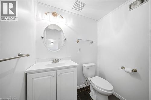 Contemporary bathroom featuring a white vanity with integrated sink, brushed nickel faucet, oval mirror, and dark tile flooring - 2306 Devon Road, Oakville, ON 