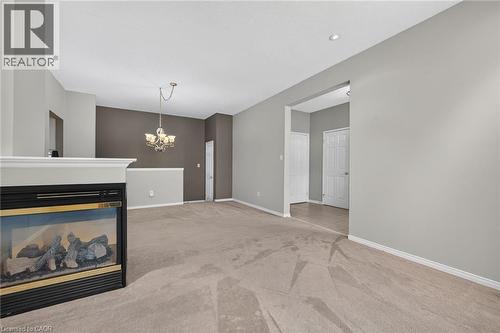 Carpeted living area featuring a built-in fireplace with a mantel, recessed lighting, and a suspended chandelier - 159 Thoroughbred Boulevard, Ancaster, ON 