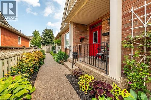 Brick exterior with a vibrant red entry door, covered porch with exposed aggregate concrete and black railing. - 159 Thoroughbred Boulevard, Ancaster, ON 