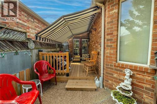 Brick exterior with a manual awning, wood deck, and French doors leading to the dinette. - 159 Thoroughbred Boulevard, Ancaster, ON 