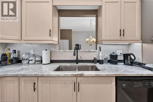 Dual basin stainless steel sink with a matte black faucet, light tone cabinetry, patterned tile backsplash, and stone-look countertops - 159 Thoroughbred Boulevard, Ancaster, ON 