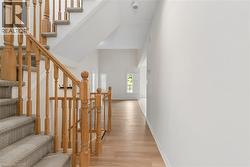 Wood-finish flooring, two-story ceiling, natural wood staircase, carpeted stair treads, and white plantation shutters - 
