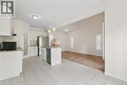 Kitchen featuring white cabinetry, stainless steel appliances, a kitchen island with sink, and tile flooring - 