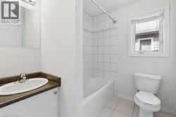 Bathroom featuring a white vanity with an integrated sink, dark countertop, and a shower-tub combination with white tile surround - 