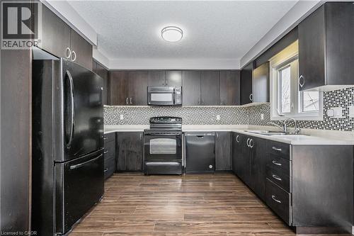 Kitchen featuring dark wood-finish cabinetry, white countertops, a mosaic tile backsplash, wood-finish flooring, and black appliances - 224 Jessica Crescent Unit# B, Kitchener, ON 