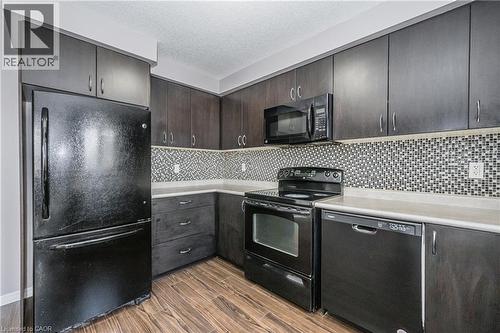 Dark wood-finish cabinetry, black appliances, mosaic tile backsplash, light countertops, and wood-finish flooring - 224 Jessica Crescent Unit# B, Kitchener, ON 