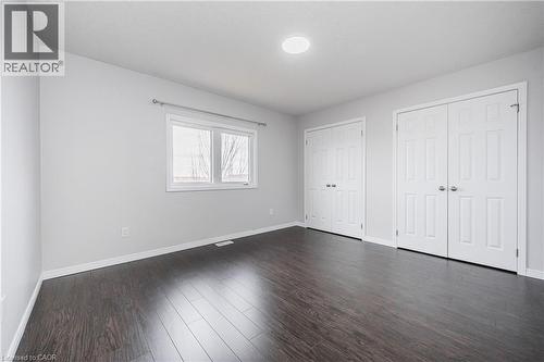 Dark wood-finish flooring, white walls, two windows, two sets of white bi-fold doors, and recessed ceiling lighting - 224 Jessica Crescent Unit# B, Kitchener, ON 