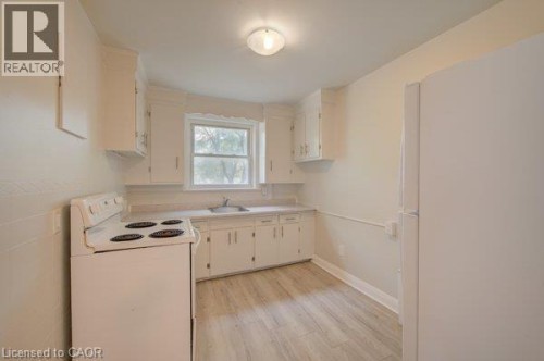 Kitchen featuring wood-finish flooring, white cabinetry, a single basin sink, a window, and a ceiling-mounted light fixture - 141 Chapel Street, Kitchener, ON 