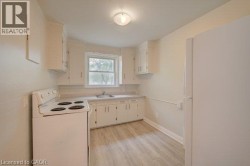 Kitchen featuring wood-finish flooring, white cabinetry, a single basin sink, a window, and a ceiling-mounted light fixture - 