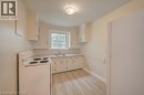 Kitchen featuring wood-finish flooring, white cabinetry, a single basin sink, a window, and a ceiling-mounted light fixture - 141 Chapel Street, Kitchener, ON 