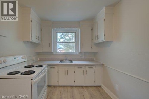 White cabinetry, built-in sink, electric range, light-toned countertops, and wood-finish flooring - 141 Chapel Street, Kitchener, ON 