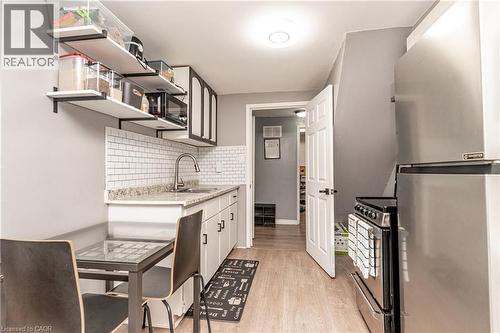 Kitchen featuring white subway tile backsplash, light-toned wood-finish flooring, white cabinetry with dark pulls, open shelving, and a stainless steel refrigerator - 52 Charters Road, Brampton, ON 