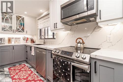 White cabinetry, gray lower cabinetry, stainless steel appliances, patterned backsplash, and under-cabinet lighting - 52 Charters Road, Brampton, ON 