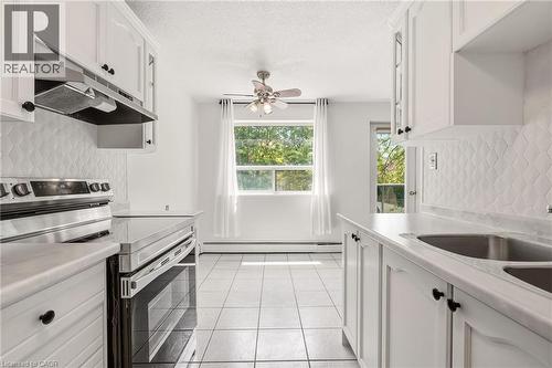 Kitchen featuring white cabinetry with black hardware, stainless steel appliances, a double basin sink, and white tiled flooring - 2411 New Street Unit# 201, Burlington, ON 