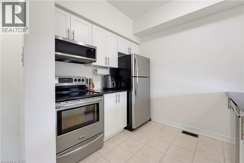 Kitchen with white cabinetry, stainless steel appliances, dark countertops, and light-toned tile flooring - 541 Winston Road Unit# 50, Grimsby, ON 