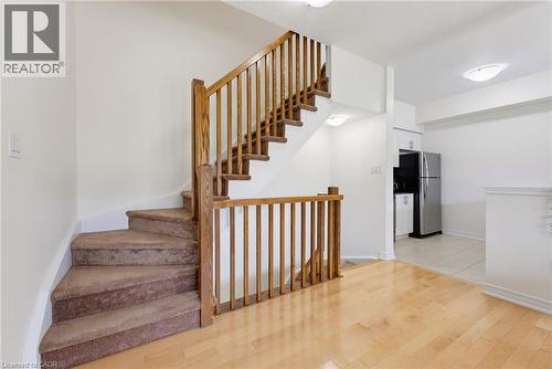 Light wood-finish flooring, wood staircase railing, carpeted stairs, recessed lighting, and stainless steel refrigerator - 541 Winston Road Unit# 50, Grimsby, ON 