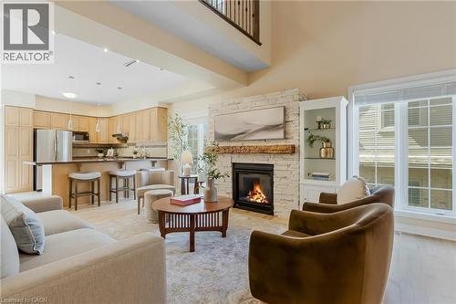 Open-concept living space featuring a stacked stone fireplace with a substantial wood mantel, built-in display cabinetry, and a kitchen with stainless steel appliances - 227 Chestnut Hill Crescent, Kitchener, ON 