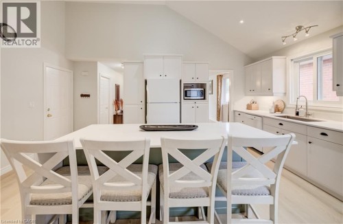 Vaulted ceiling kitchen featuring white cabinetry, light-toned wood-finish flooring, a central island with countertop seating, and a stainless steel sink with a gooseneck faucet - 245 Fern Crescent, Waterloo, ON 