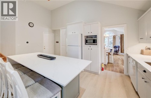 Bright, modern kitchen featuring a generous white quartz island with seating, stainless steel built-in appliances including a wall-mounted microwave, white cabinetry with hardware accents, light wood- - 245 Fern Crescent, Waterloo, ON 