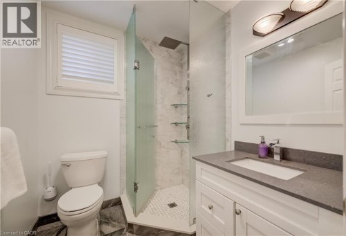 Bathroom featuring a glass-enclosed shower with a rain showerhead, a white vanity with a gray countertop, a rectangular sink, and a white framed mirror with an overhead light fixture - 245 Fern Crescent, Waterloo, ON 