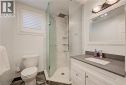 Bathroom featuring a glass-enclosed shower with a rain showerhead, a white vanity with a gray countertop, a rectangular sink, and a white framed mirror with an overhead light fixture - 