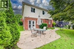 Brick and siding exterior featuring a concrete patio, mature trees, and privacy hedging - 
