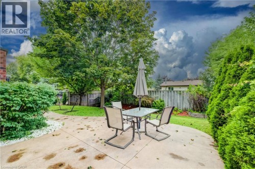 Concrete patio with a curved edge, surrounded by mature trees and shrubs - 245 Fern Crescent, Waterloo, ON 