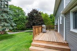 Wood deck with railing and steps to the lawn, gray horizontal siding, white trim around windows, and a white downspout - 