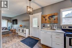 Wood-finish flooring throughout, white paneled entry door with decorative glass, recessed lighting, white cabinetry with silver hardware, and stone-look countertops - 