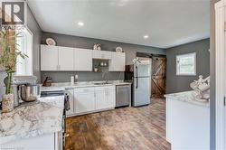 Kitchen featuring white cabinetry, light-toned countertops, stainless steel appliances, wood-finish flooring, and a rustic barn door - 