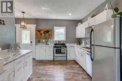 White cabinetry with brushed nickel hardware, marbling countertops, stainless steel appliances, wood-finish flooring, and a decorative glass paneled entry door - 