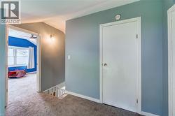 Carpeted hallway with a wall-mounted light fixture, leading to a bedroom with a ceiling fan and window - 