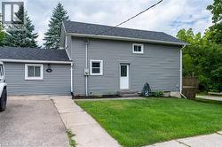 Gray siding exterior with dark shingle roofing, featuring a concrete walkway and a green lawn - 